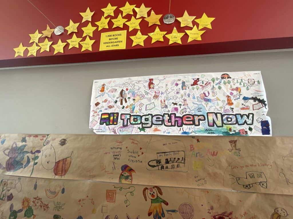 Pictured is an "All Together Now" banner, decorated by child patrons.