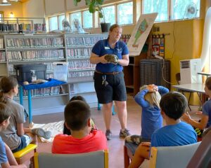 An educator from the New Mexico Wildlife Center holds up a turtle to show the children attending the Summer Reading Camp.