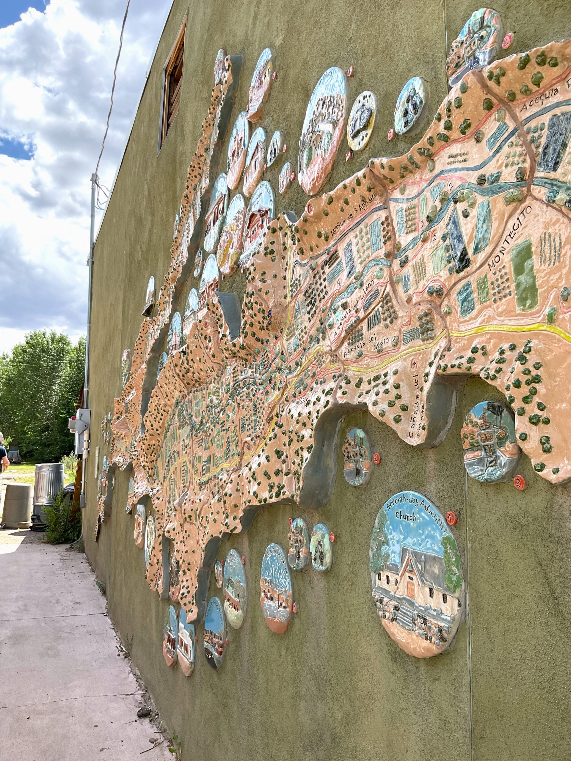 An angled view of the ceramic mural on the side of the Dixon Cooperative Market & Deli. The mural shows important landmarks in Dixon, including their acequias.