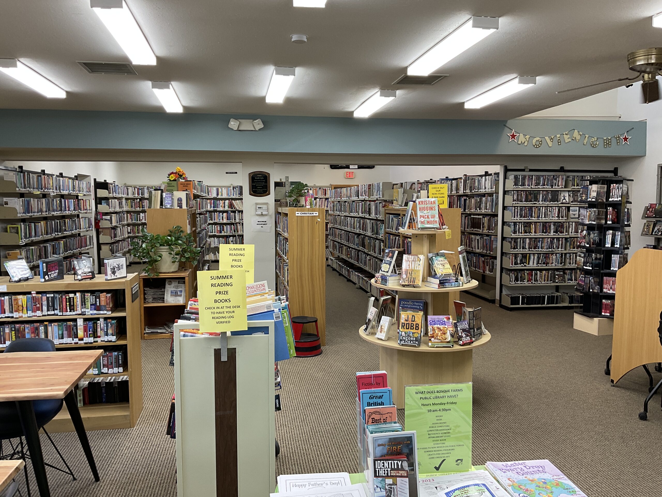 A view of the inside of Bosque Farms library showing book shelves and displays along with a "summer reading prize books" cart.
