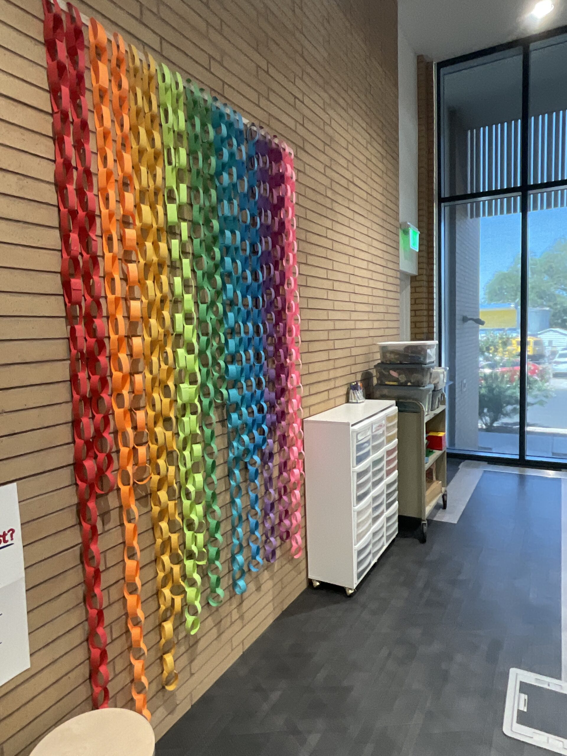 Colored strings of paper links are displayed in an order than resembles a rainbow. Beside it are bins and shelves of craft supplies and Legos. 